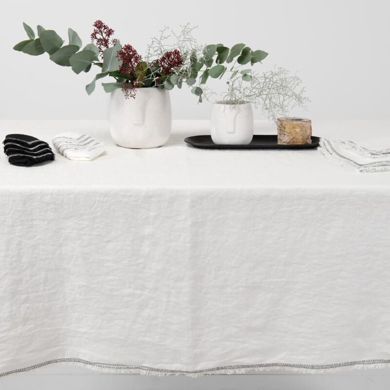 white linen tablecloth with decorative seam with loose fringes.